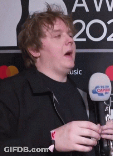 A Man Holding A Microphone In Front Of A Sign That Says Music GIF