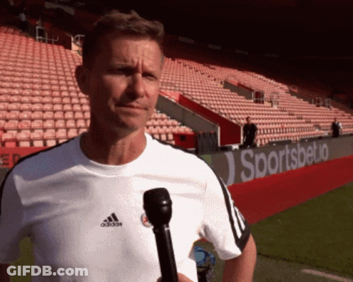 A Man Holding A Microphone In Front Of A Sportsbetio Ad GIF