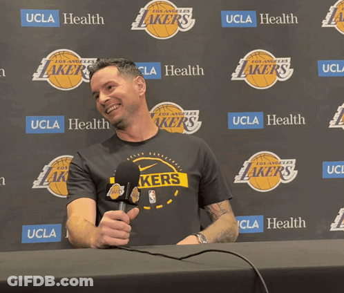 A Man Holding A Microphone In Front Of A Wall That Says Lakers GIF
