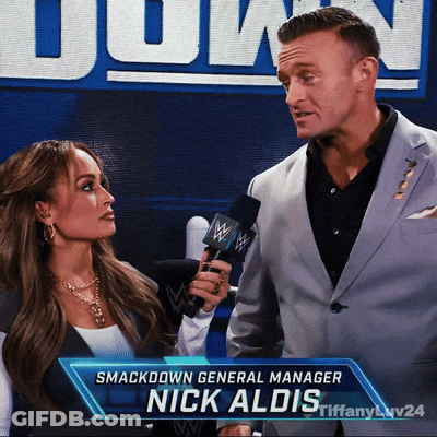 A Man Holding A Microphone Next To A Woman With The Name Nick Aldis GIF