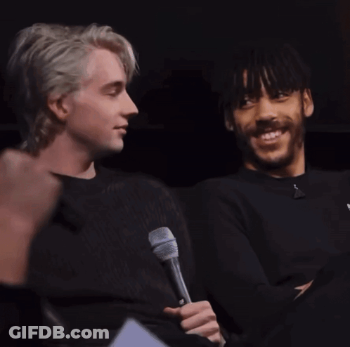 A Man Holding A Microphone Next To Another Man Who Is Smiling GIF
