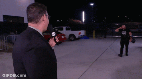 A Man Holding A Microphone That Says Tnt Stands In A Parking Lot GIF