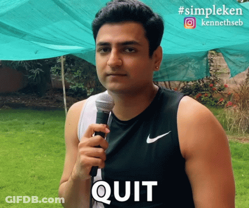 A Man Holding A Microphone With The Word Quit Written On His Shirt GIF