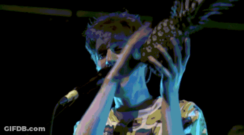 A Man Holding A Pineapple In Front Of His Face While Singing Into A Microphone GIF