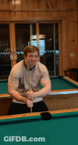 A Man Holding A Pool Cue On A Pool Table In Front Of A Window With The Number 00 On It GIF