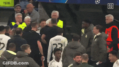 A Man Holding A Red Card Stands In A Crowd Of People GIF