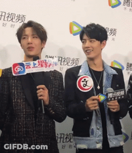 A Man Holding A Sign That Says ' A ' On It Stands Next To Another Man GIF