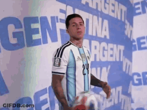 A Man Holding A Soccer Ball In Front Of A Sign That Says Argentina GIF