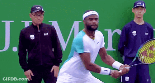 A Man Holding A Tennis Racquet In Front Of A Sign That Says J.m. GIF