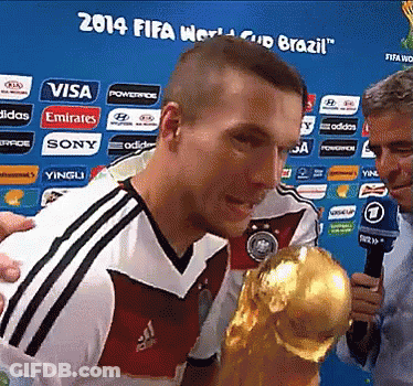 A Man Holding A Trophy In Front Of A 2014 Fifa World Cup Brazil Banner GIF