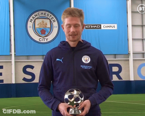A Man Holding A Trophy In Front Of A Manchester City Sign GIF