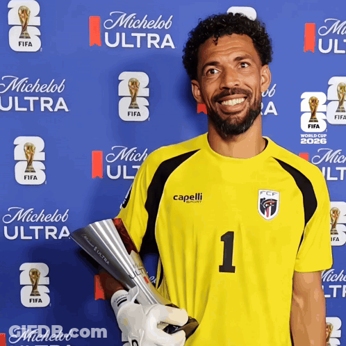 A Man Holding A Trophy In Front Of A Wall That Says Michelob Ultra GIF