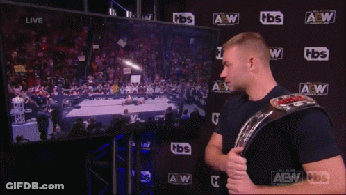 A Man Holding A Wrestling Belt Stands In Front Of A Screen That Says Tbs GIF