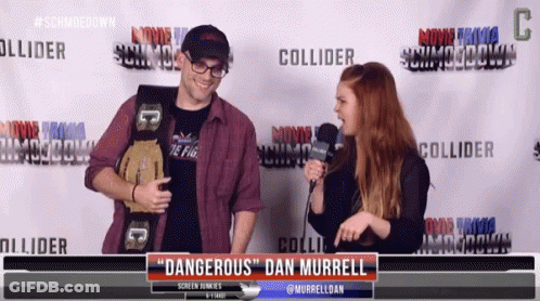 A Man Holding A Wrestling Belt Talks To A Woman In Front Of A Screen That Says " Dangerous " Dan Murrell GIF