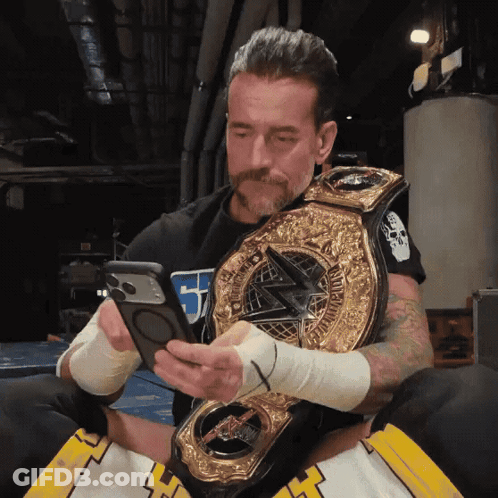 A Man Holding A Wrestling Championship Belt Looking At His Phone GIF