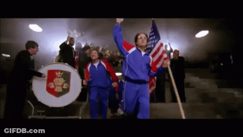 A Man Holding An American Flag Stands In Front Of A Drum With A Crown On It GIF