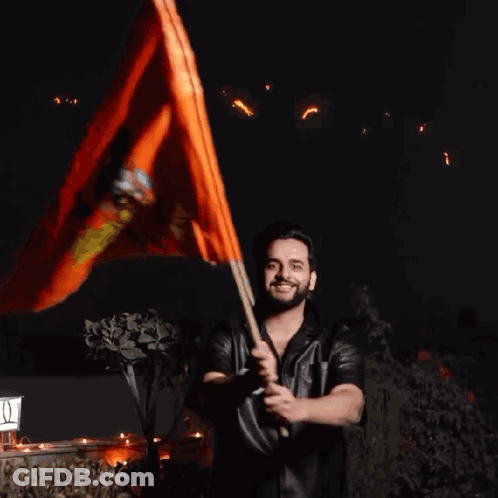 A Man Holding An Orange Flag In Front Of A Sign That Says ' I ' On It GIF