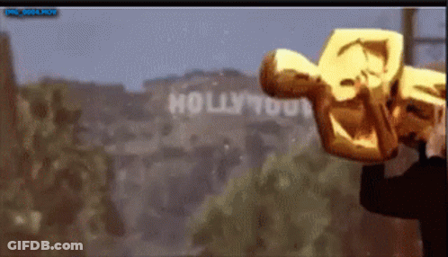 A Man Holding An Oscar Statue In Front Of A Hollywood Sign GIF