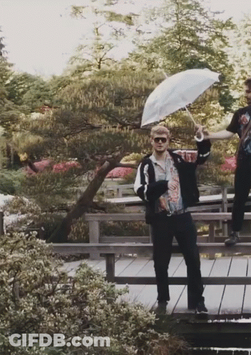 A Man Holding An Umbrella Is Standing On A Wooden Bridge GIF