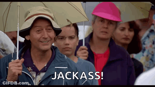A Man Holding An Umbrella Says Jackass In A Crowd GIF