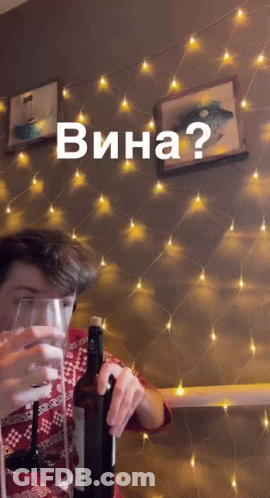 A Man Holds A Bottle Of Wine In Front Of A String Of Lights With The Words Wina Written On It GIF