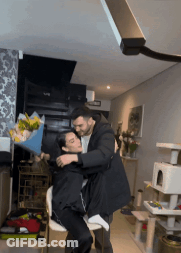 A Man Holds A Bouquet Of Flowers Over A Woman 'S Head GIF