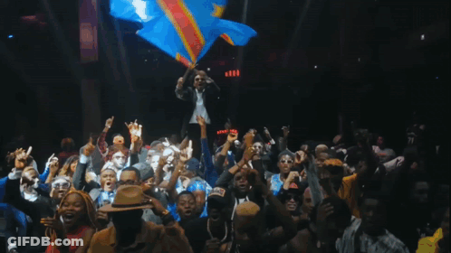 A Man Holds A Flag In Front Of A Crowd Of People GIF