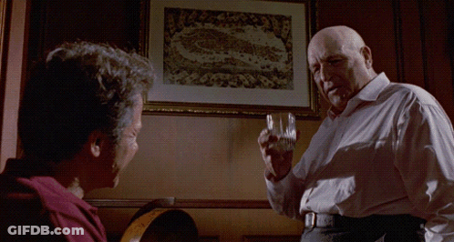 A Man Holds A Glass In Front Of A Framed Picture That Says Juicy GIF