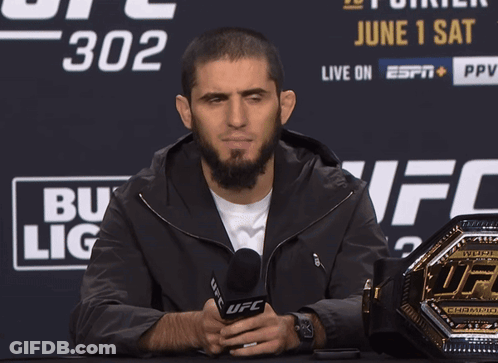 A Man Holds A Microphone In Front Of A Ufc Championship Belt GIF