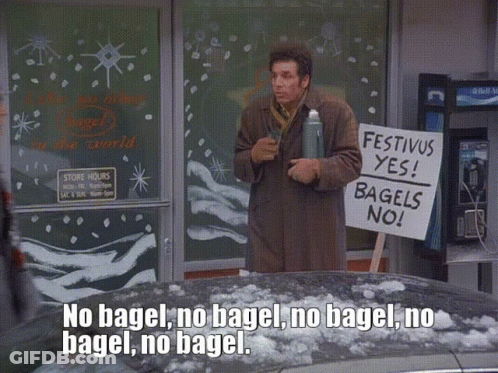 A Man Holds A Sign That Says Festivus Yes Bagels No GIF
