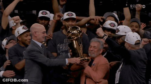 A Man Holds A Trophy In Front Of A Group Of Basketball Players GIF