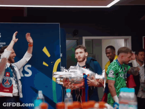 A Man Holds A Trophy In Front Of A Wall That Says Champions League GIF