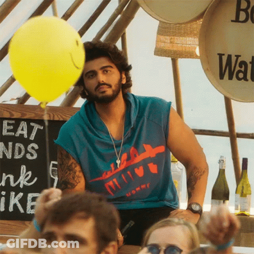 A Man Holds A Yellow Balloon In Front Of A Sign That Says Eat And Drink GIF