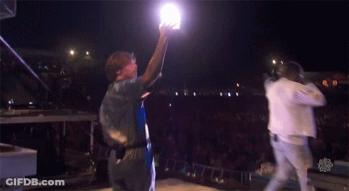 A Man Holds Up A Light While Standing On A Stage GIF