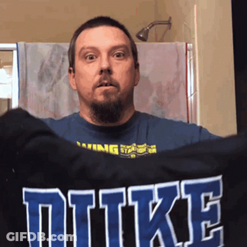 A Man Holds Up A Shirt That Says Duke GIF