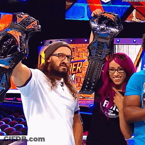 A Man Holds Up Two Championship Belts While Standing Next To A Woman GIF