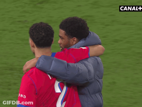 A Man Hugging Another Man On A Soccer Field With Canal + In The Background GIF
