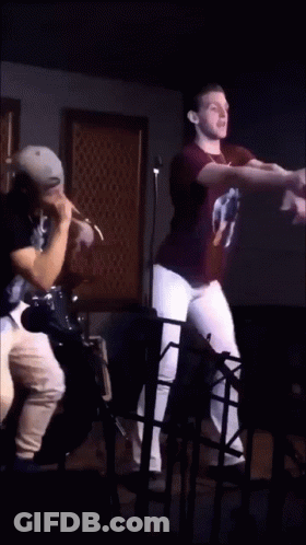 A Man In A 2Pac Shirt Stands Next To Another Man In A Black Shirt GIF