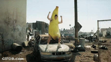 A Man In A Banana Costume Is Standing In Front Of A Broken Car . GIF