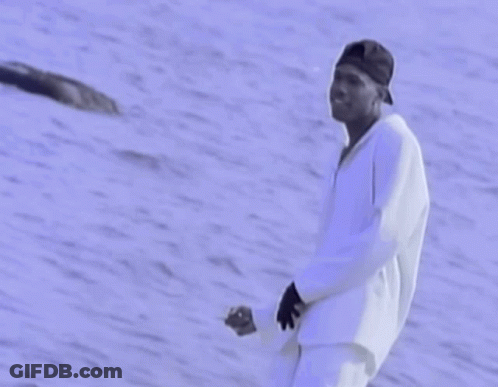 A Man In A Baseball Cap Is Standing In Front Of A Body Of Water GIF