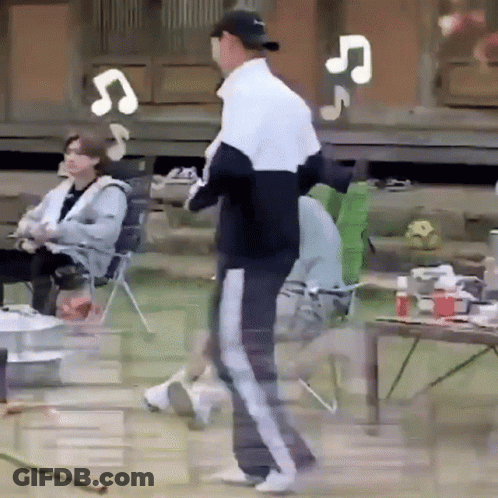 A Man In A Baseball Cap Is Standing In Front Of A Group Of People Sitting In Chairs And A Table . GIF
