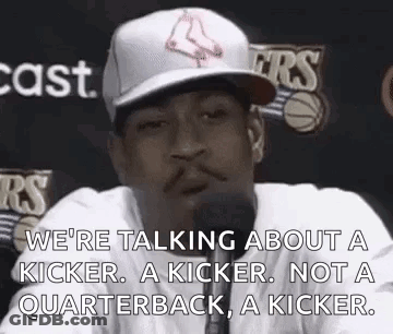 A Man In A Baseball Cap Is Talking Into A Microphone While Wearing A White Shirt . GIF