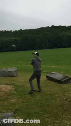 A Man In A Baseball Cap Stands In A Field With A Grave In The Background GIF