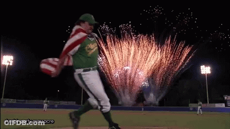 A Man In A Baseball Uniform Is Running With An American Flag In Front Of Fireworks .. GIF