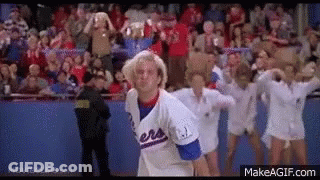A Man In A Baseball Uniform Is Standing In Front Of A Crowd Of Cheerleaders In A Stadium . GIF