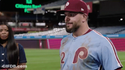 A Man In A Baseball Uniform Is Standing On A Baseball Field With A Woman In The Background . GIF