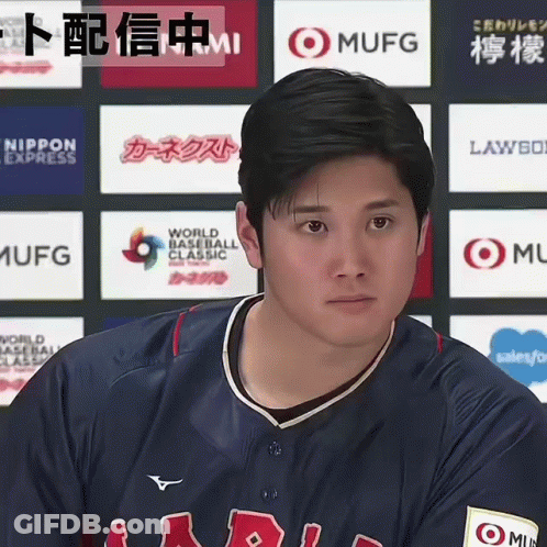 A Man In A Baseball Uniform Stands In Front Of A Wall Of Logos Including One For Mufg GIF