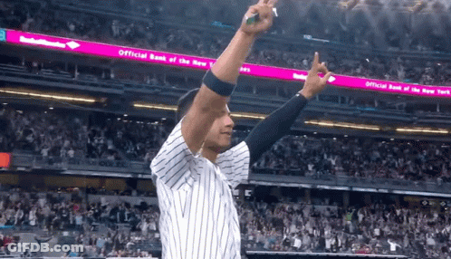 A Man In A Baseball Uniform Stands In Front Of An Official Bank Of The New York Sign GIF