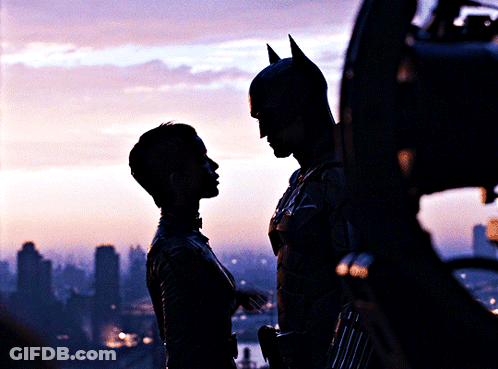 A Man In A Bat Suit Stands Next To A Woman In A Silhouette GIF