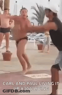 A Man In A Bathing Suit Is Dancing With Another Man In A Hat . GIF
